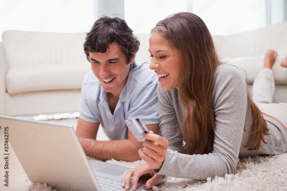 Couple lying on the floor with laptop booking holidays Couple lying on the floor with laptop booking holidays