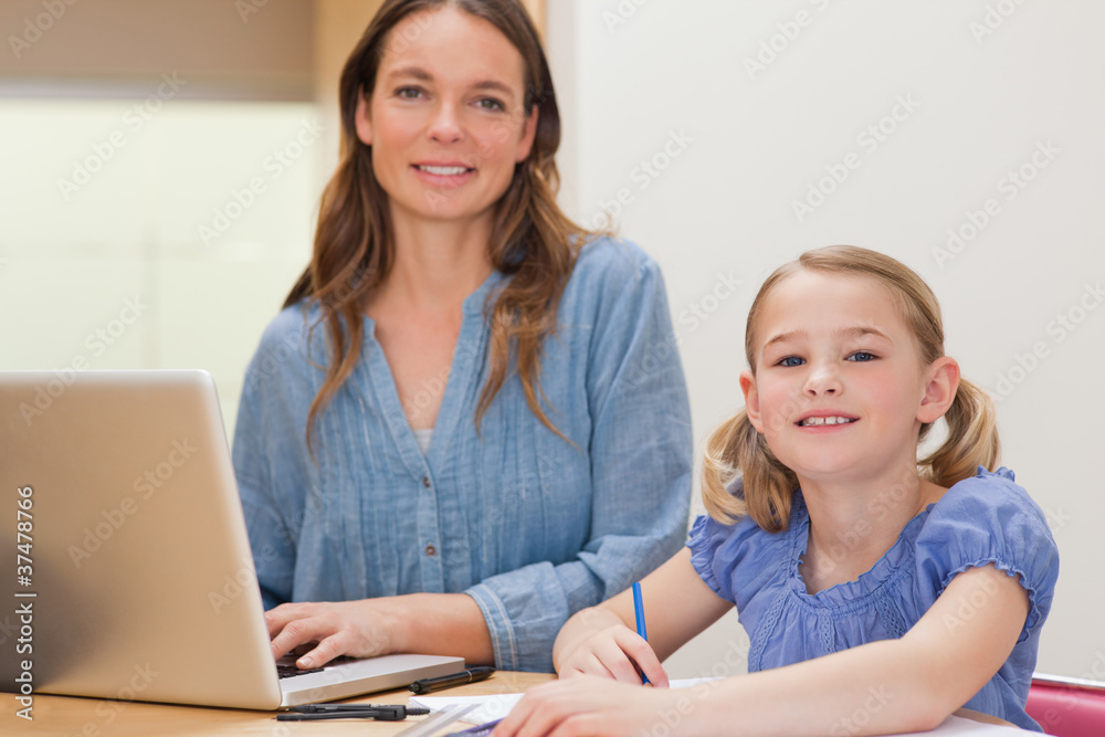 Girl doing her homework while her mother is using notebook Girl doing her homework while her mother is using notebook