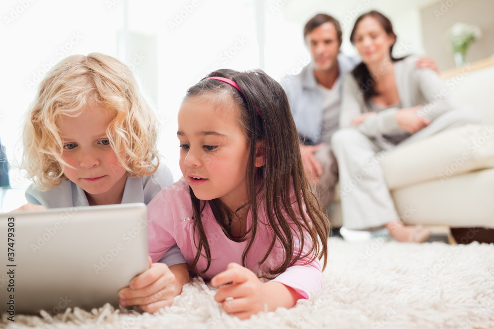 Cute siblings using a tablet computer while their parents are in Cute siblings using a tablet computer while their parents are in