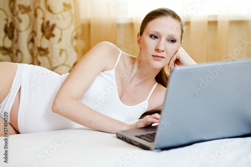 pregnant woman relaxing with her laptop on a bed at home