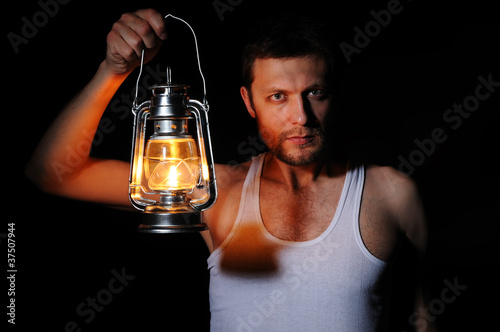 Fotografie Man with a kerosene lamp on black background