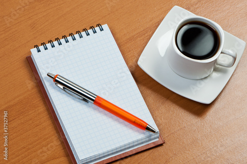 Notebook with pen and coffee on table.