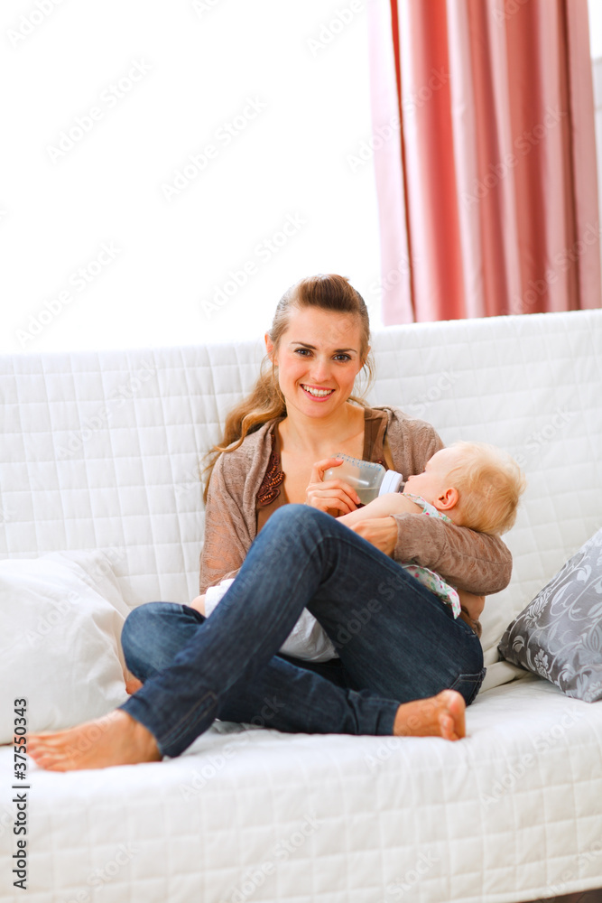 Young mother sitting on sofa and feeding her baby Young mother sitting on sofa and feeding her baby