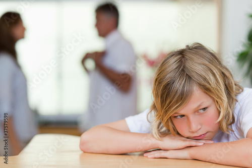 Sad looking boy with fighting parents behind him