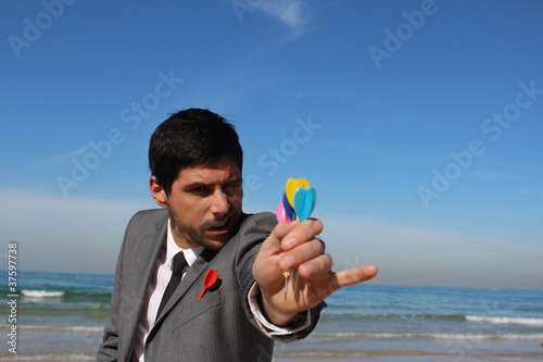 Young handsome businessman throws darts at the beach photo