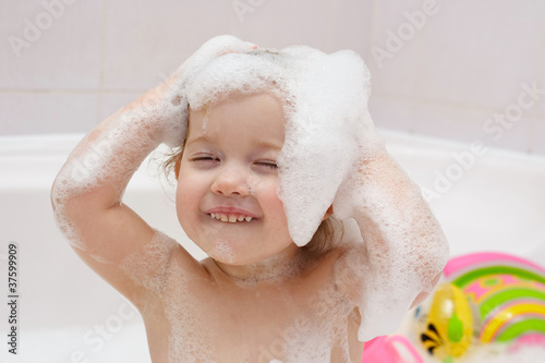 Fotografering little child is washing her hair in bath