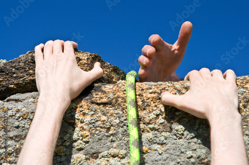 Rock climber reaching for helping-hand partner.