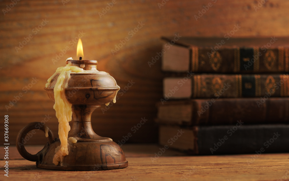 old candle on a wooden table, old books in the background old candle on a wooden table, old books in the background