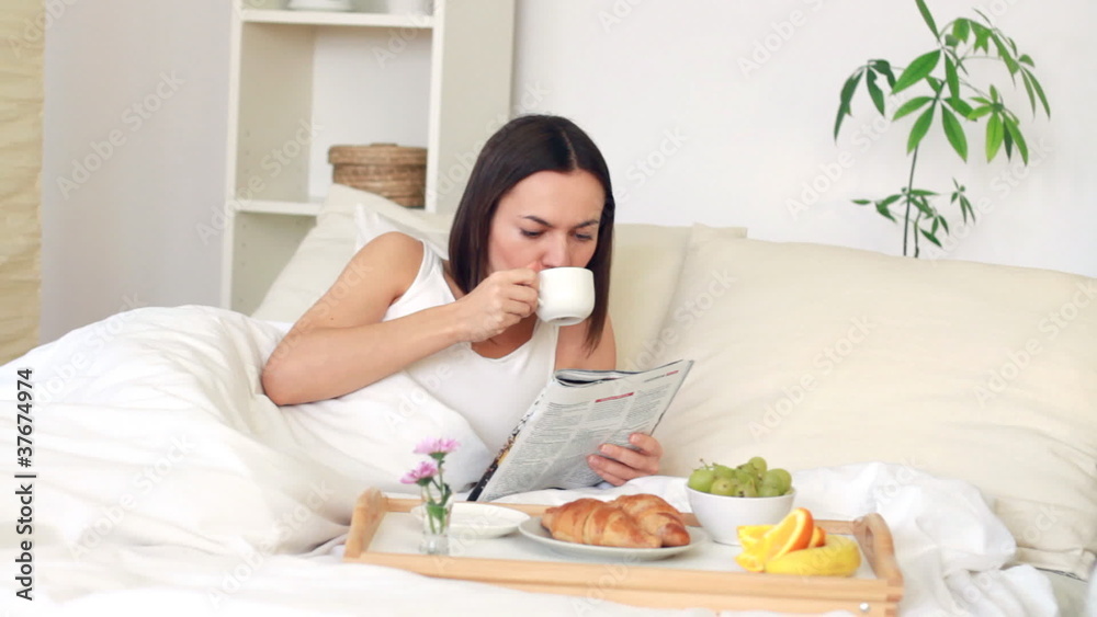 Woman eating breakfast in bed and reading magazine Woman eating breakfast in bed and reading magazine