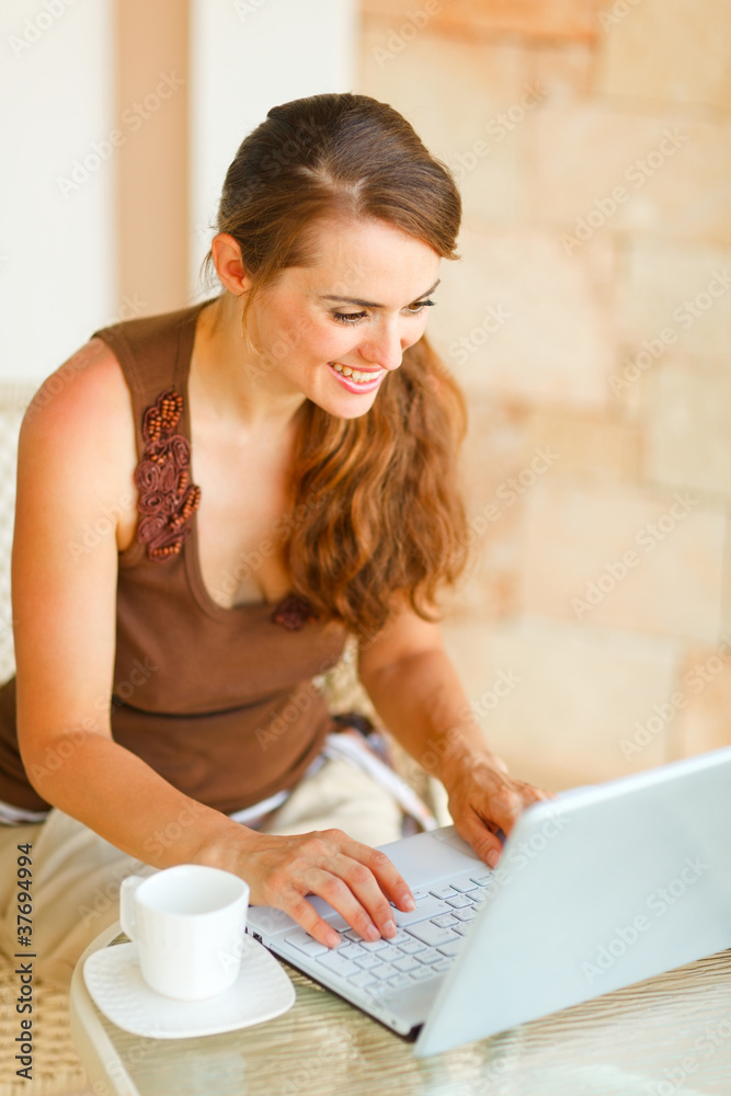 Fototapeta premium Smiling young woman with cup of coffee working on laptop