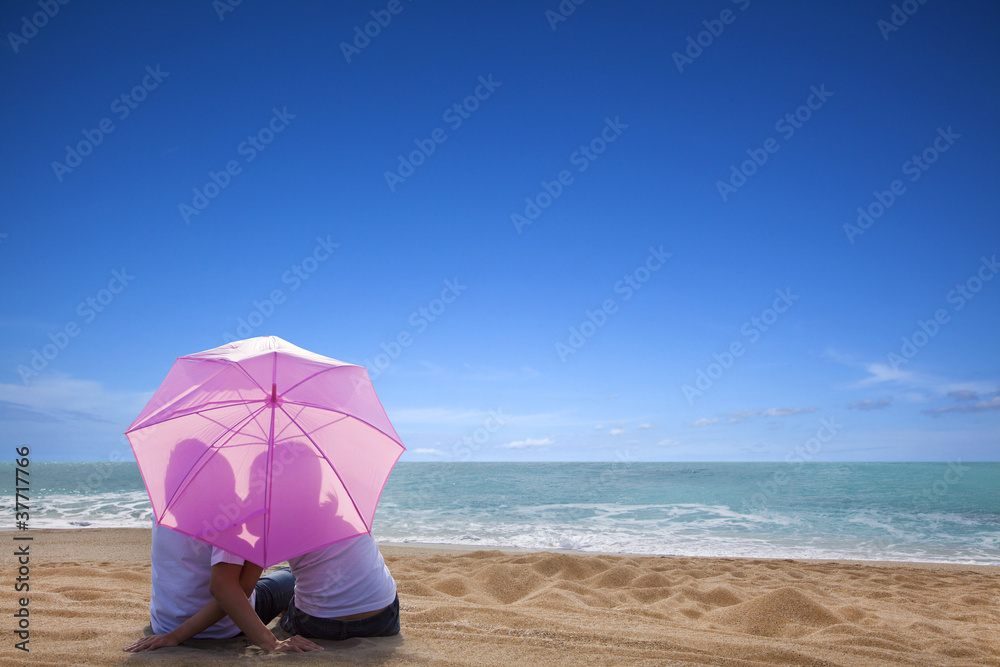 young couple kissing at the beach with the umbrella