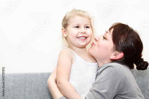 Mother and her little daughter sitting and couch and hugging