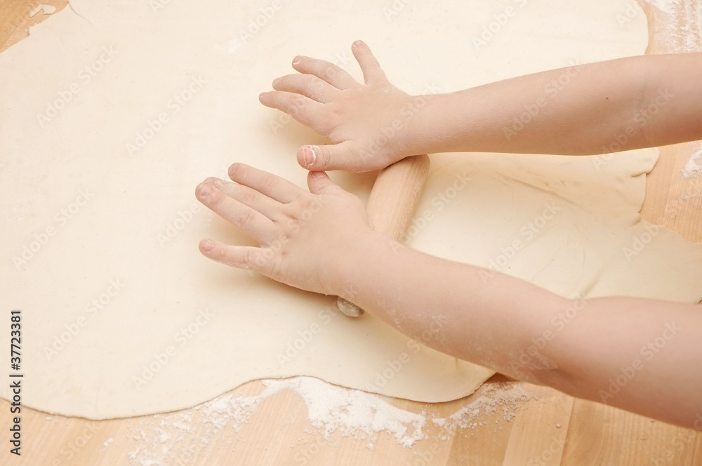 Fototapeta premium Child's hands kneading dough on wooden table