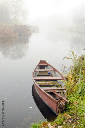 Wooden boat on coast of river sunken in dense fog.