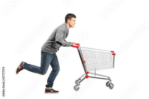 Fototapeta Young man running and pushing an empty shopping cart