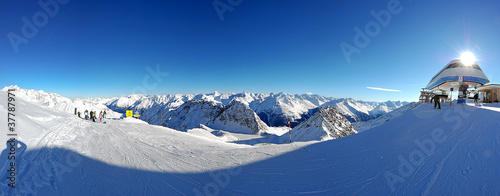 Panorama with ski trail, tall snow drifts on the slope of Tyrolean Alps and blue sky, hovering around the sharp rocky peaks.