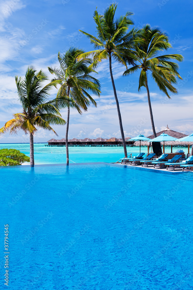 Infinity pool with umbrellas and palm trees over lagoon Infinity pool with umbrellas and palm trees over lagoon