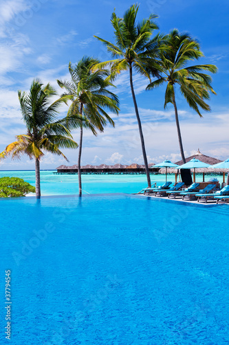 Infinity pool with umbrellas and palm trees over lagoon © Martin Valigursky
