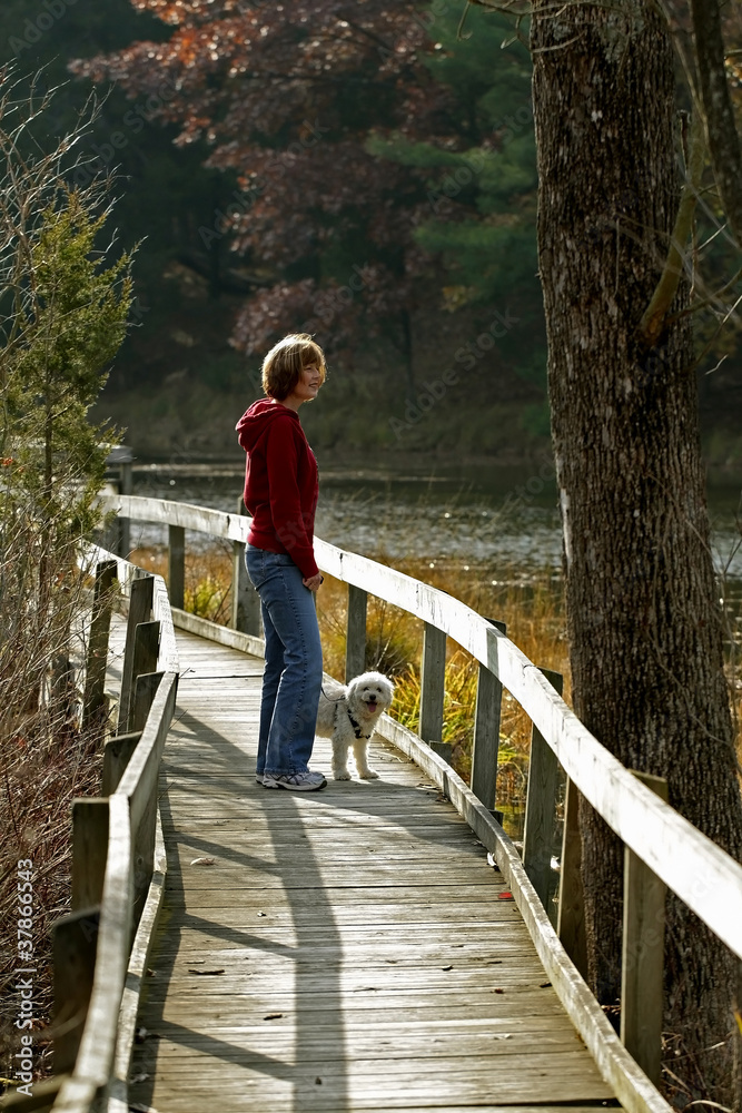 Woman and Small White Dog on Boardwalk Next to River
