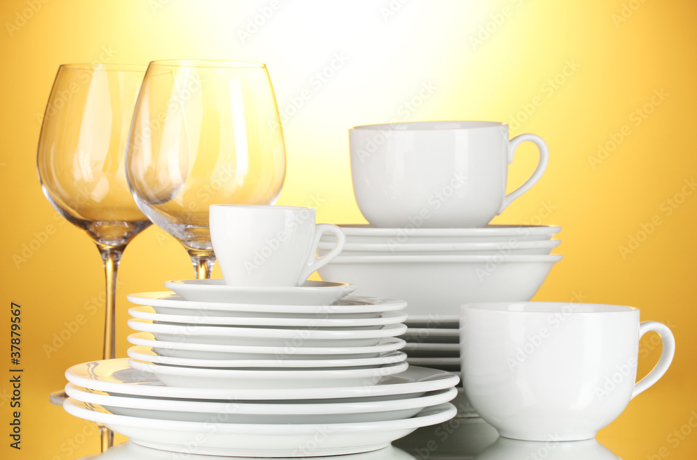 empty bowls, plates, cups and glasses on yellow background empty bowls, plates, cups and glasses on yellow background