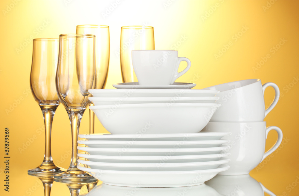 Fototapeta premium Clean white dinnerware and glassware stacked on reflective surface with golden background