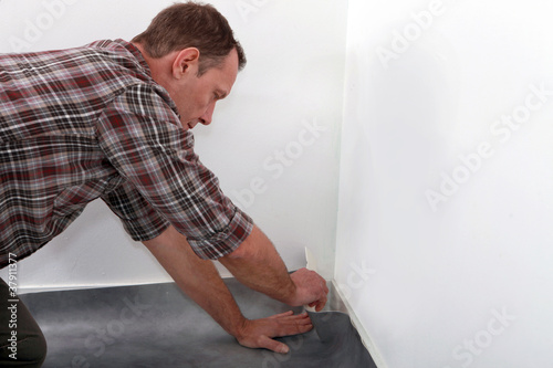 Man fitting linoleum flooring into the corner of a room © auremar