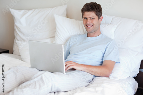 Smiling man lying in bed with laptop