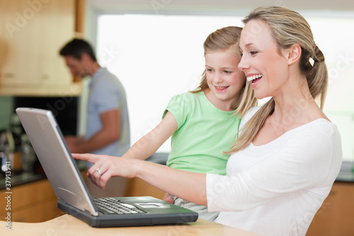 Happy mother and daughter using laptop with father in the backgr