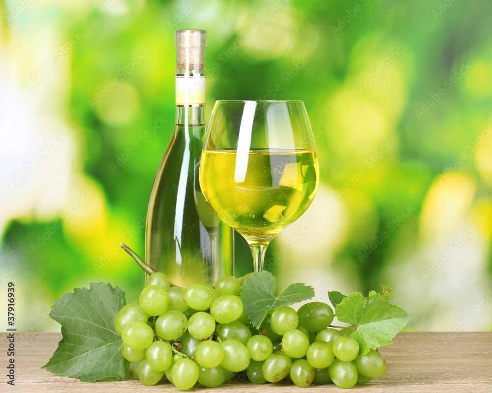 Bottle of wine, glass and grapes on green background