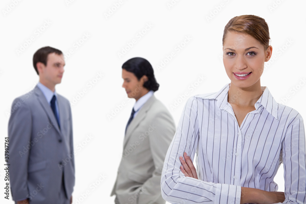 Busiensswoman with arms folded and talking colleagues behind her Busiensswoman with arms folded and talking colleagues behind her