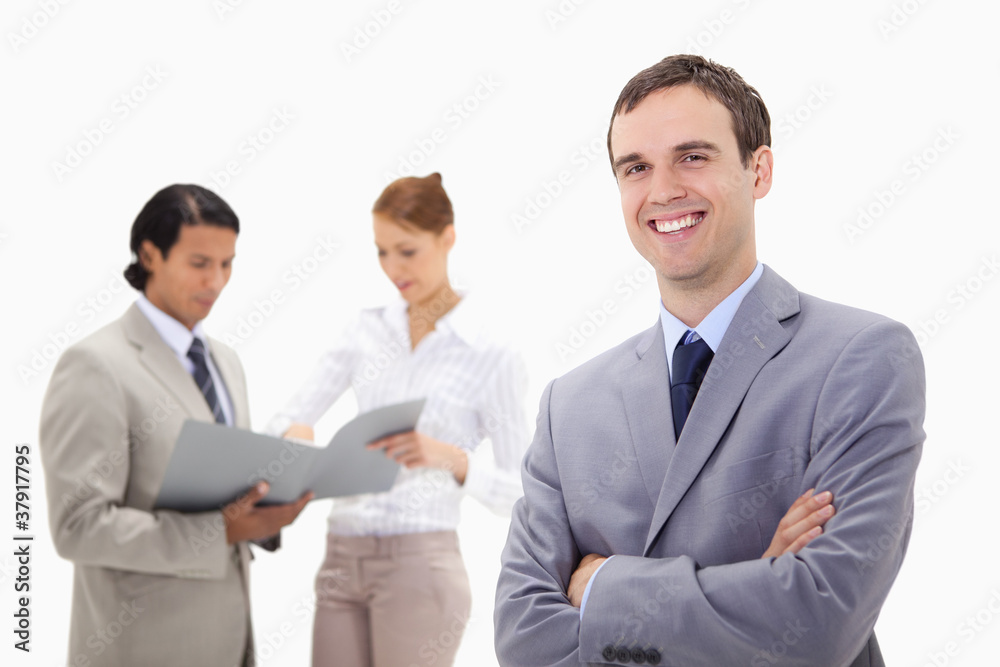 Smiling young businessman with talking colleagues behind him Smiling young businessman with talking colleagues behind him