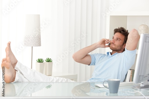 Relaxed man talking on mobile phone at desk
