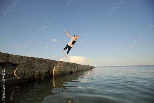 Young man jumping from a pier inro the water