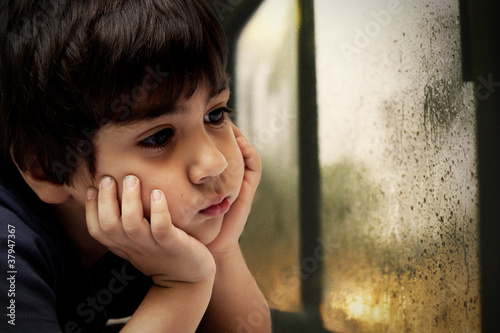 bambino che guarda la pioggia che cade dal vetro photo