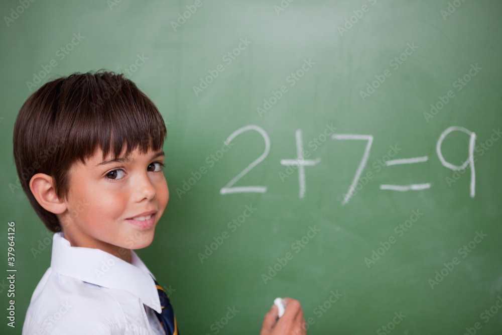 Smiling schoolboy writing an addition Smiling schoolboy writing an addition