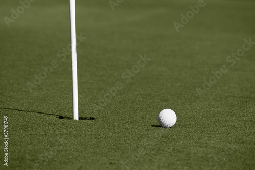 Golf ball close to hole with flagstick on putting green