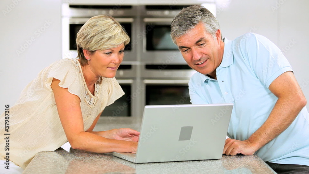 Wireless Laptop Used by Mature Couple in Kitchen Wireless Laptop Used by Mature Couple in Kitchen