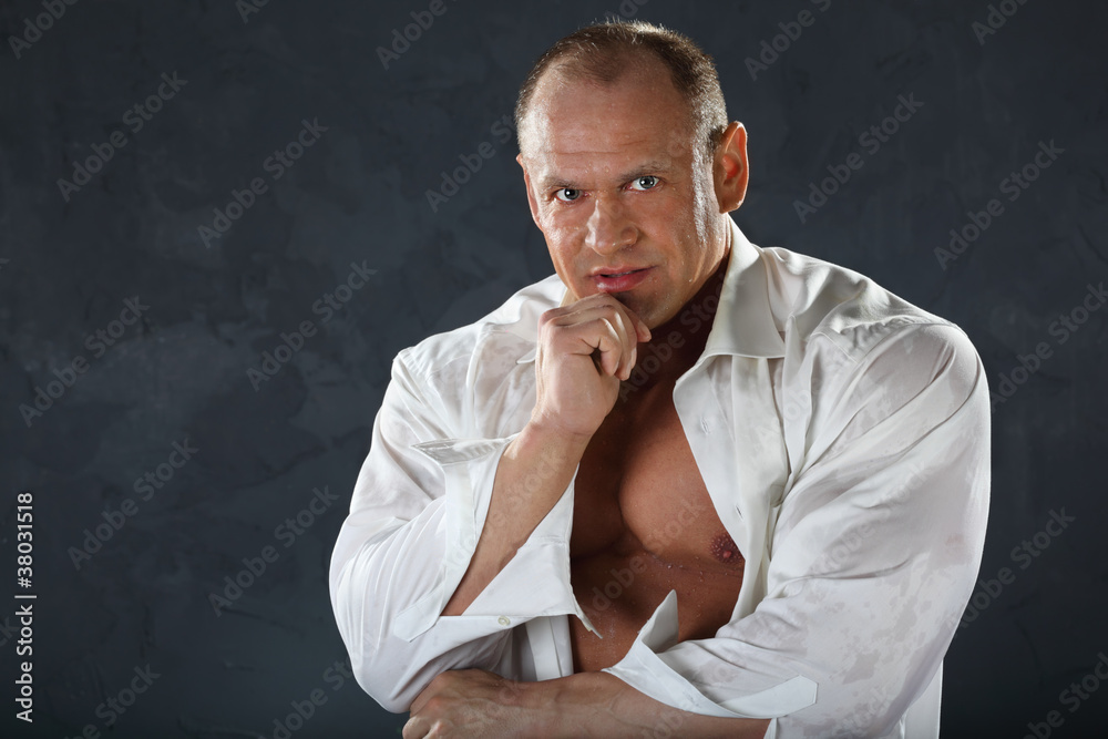Tanned bodybuilder wearing wet shirt looks thoughtfully Tanned bodybuilder wearing wet shirt looks thoughtfully