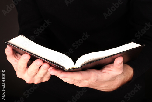 Hands holding open russian bible on black background