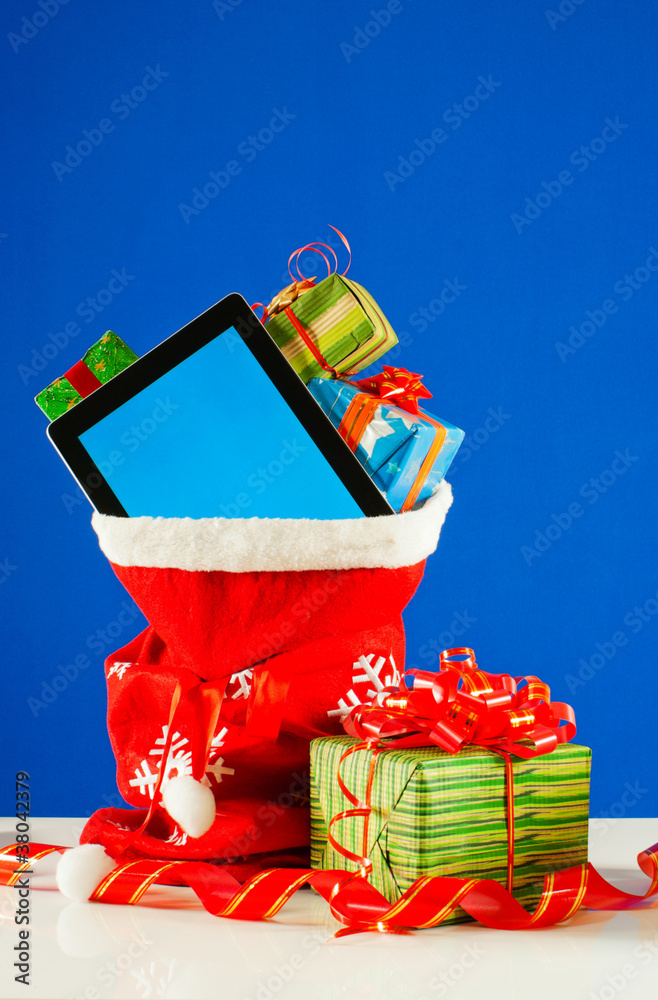 Tablet PC with heap of presents in red bag against blue backgrou