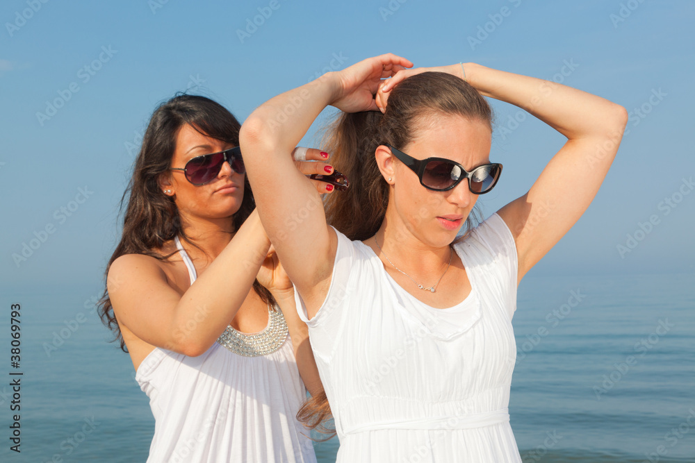 Young Woman Dress Her Friend's Hairs at Seaside Young Woman Dress Her Friend's Hairs at Seaside