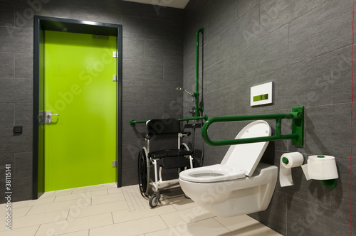 a toilet for disabled people with green bars, wheelchair