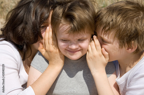 Girl and boy whispering secret to their sister.