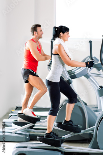 man and woman with elliptical cross trainer at gym