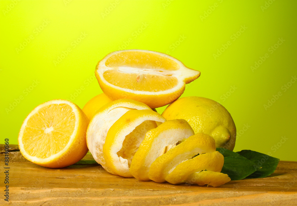 ripe lemons with leaves on wooden table on green background