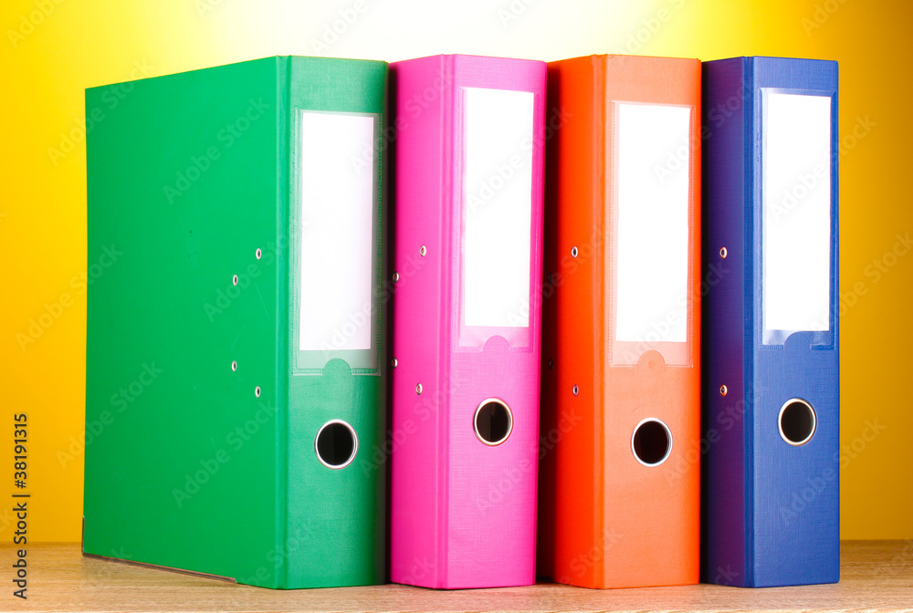 bright office folders on wooden table on yellow background. bright office folders on wooden table on yellow background.
