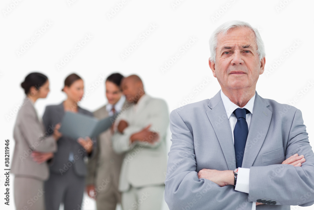 Mature salesman with arms folded and team behind him Mature salesman with arms folded and team behind him