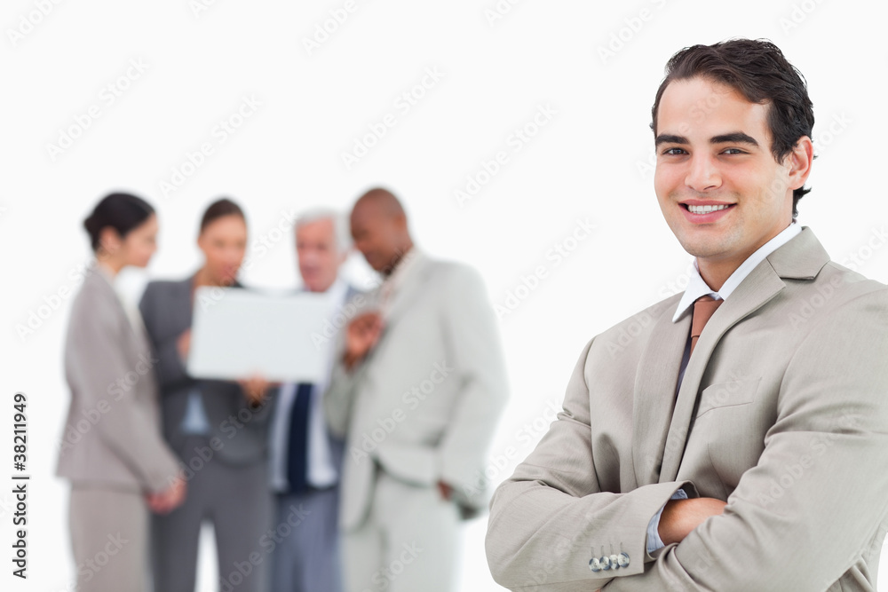 Smiling salesman with arms folded and colleagues behind him Smiling salesman with arms folded and colleagues behind him