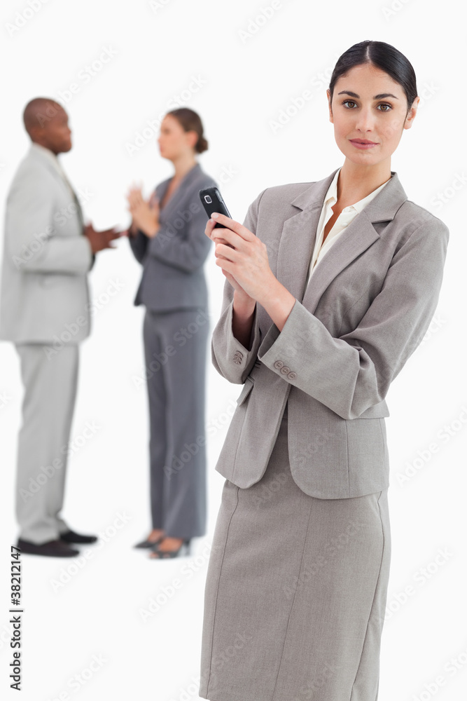 Saleswoman holding cellphone with colleagues behind her Saleswoman holding cellphone with colleagues behind her