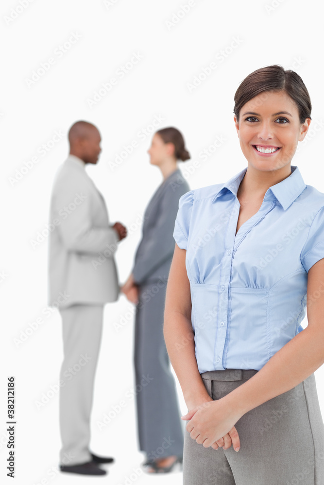 Smiling businesswoman with talking co-workers behind her Smiling businesswoman with talking co-workers behind her